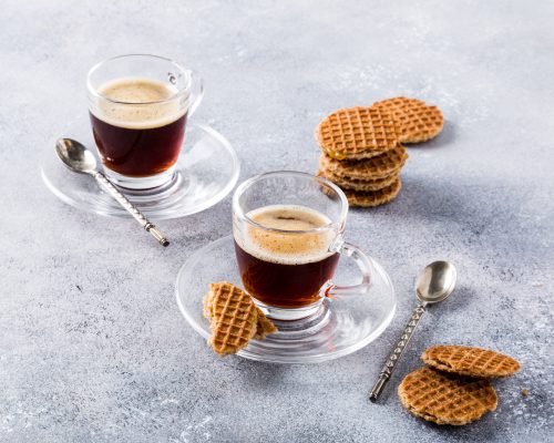 Glass cups of coffee with mini stroopwafel, syrupwaffles cookies on light gray background with copy space.